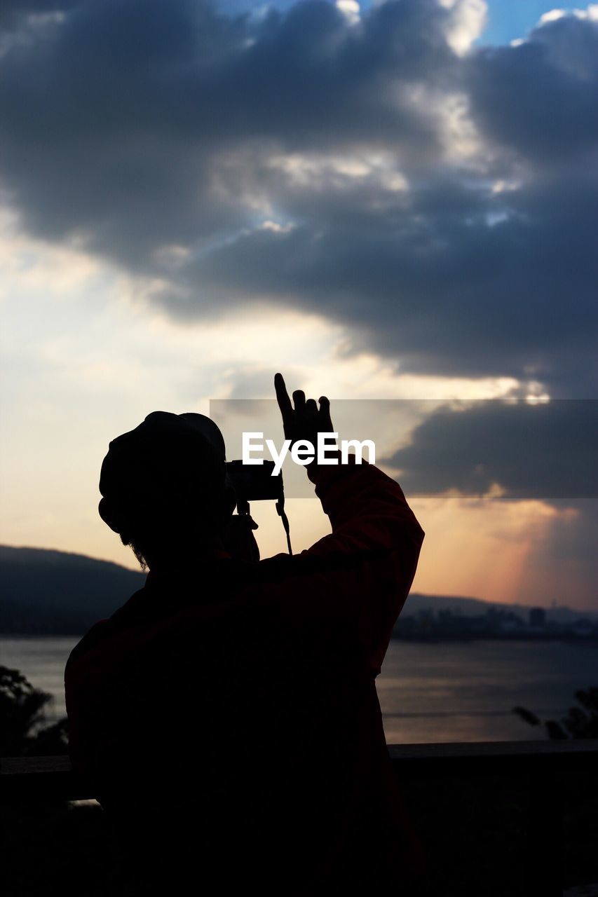 Rear view of man photographing cloudy sky during sunset
