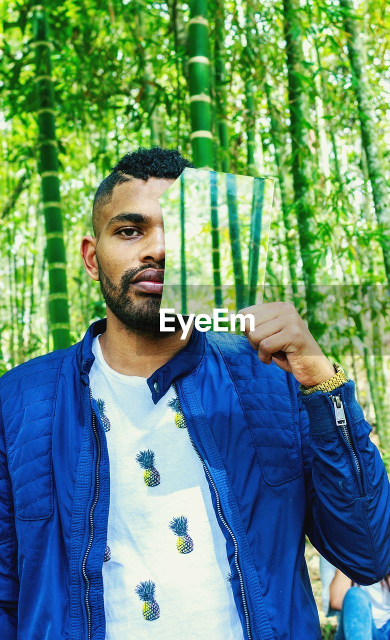 Portrait of man holding broken mirror against trees