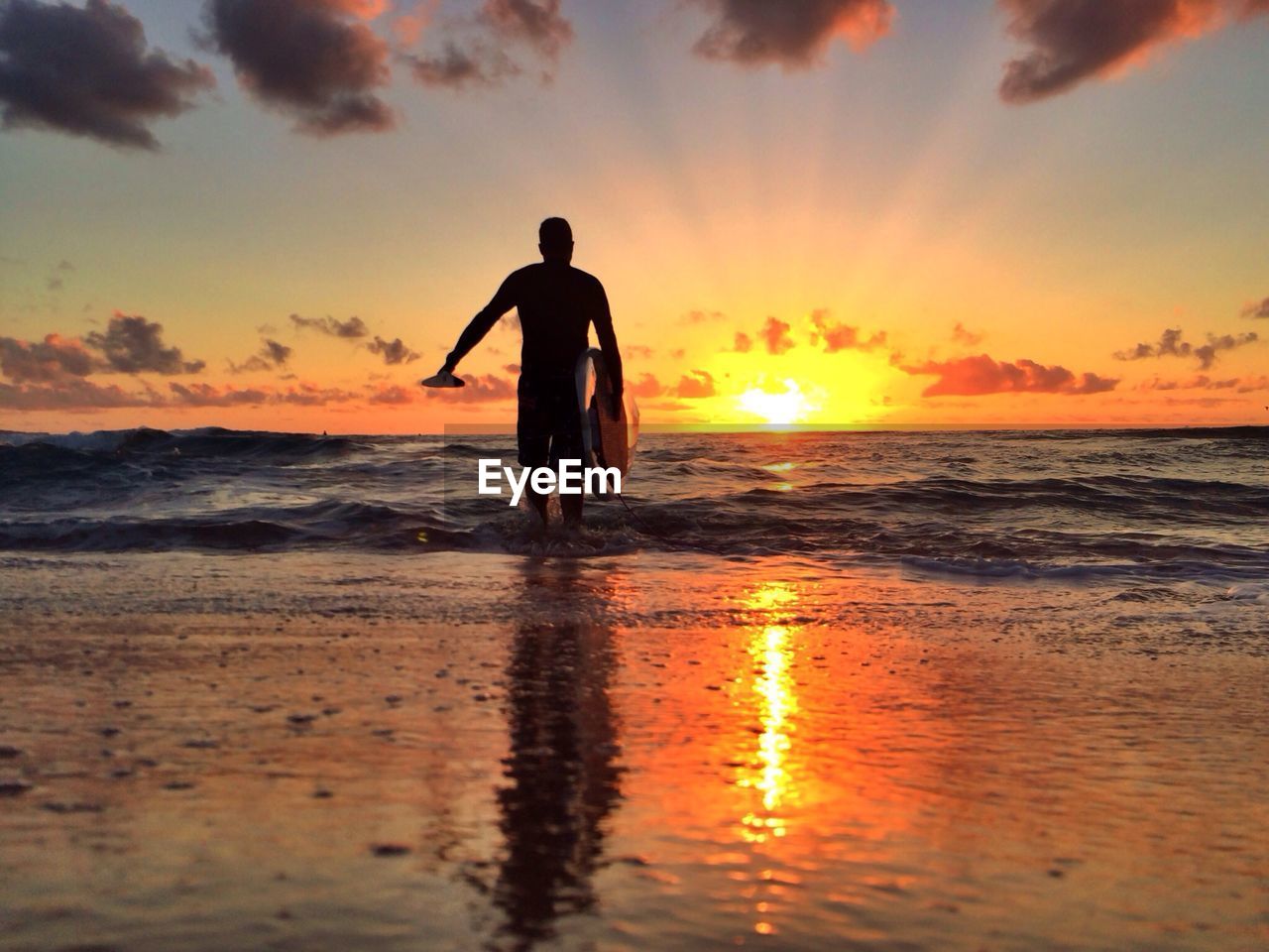 Rear view of silhouette man with surfboard walking in sea at sunset