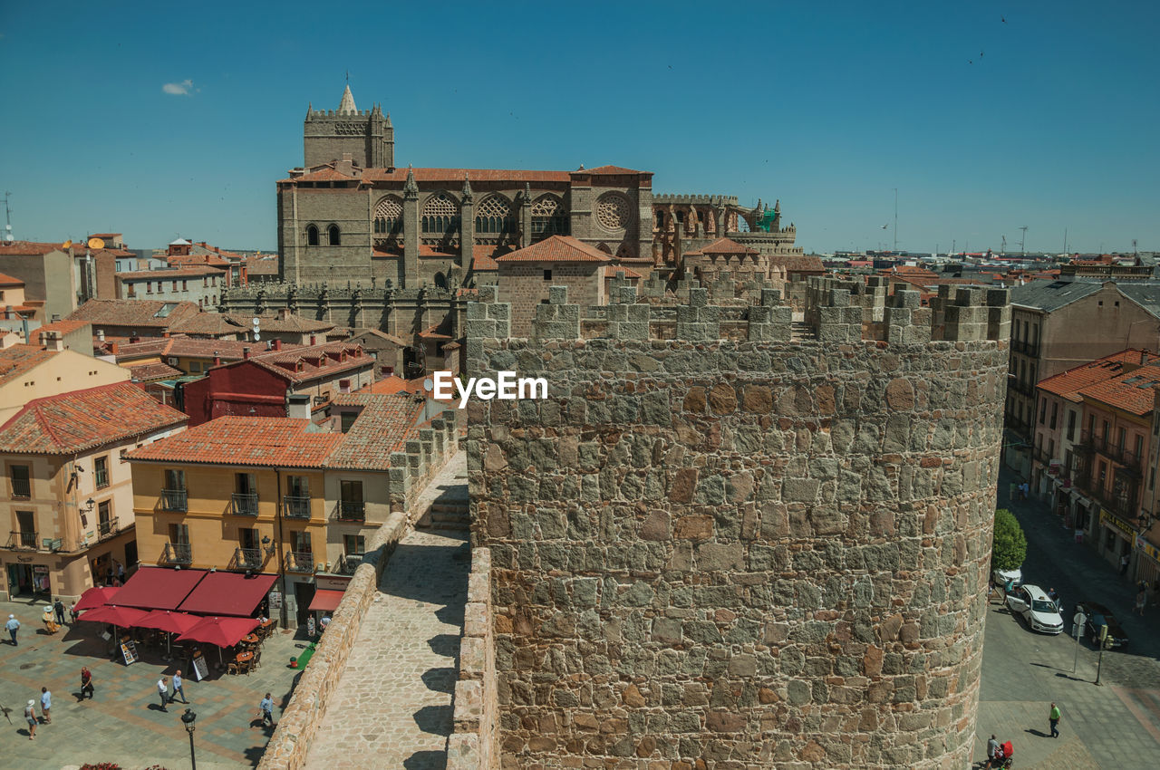 People walking on alley and pathway over wall with cathedral of avila. spain.