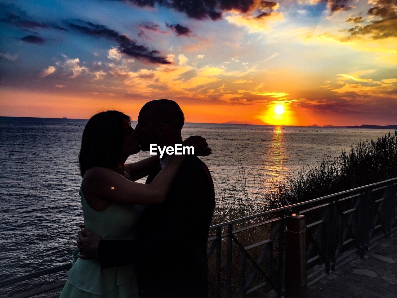 Romantic couple kissing against sea during sunset