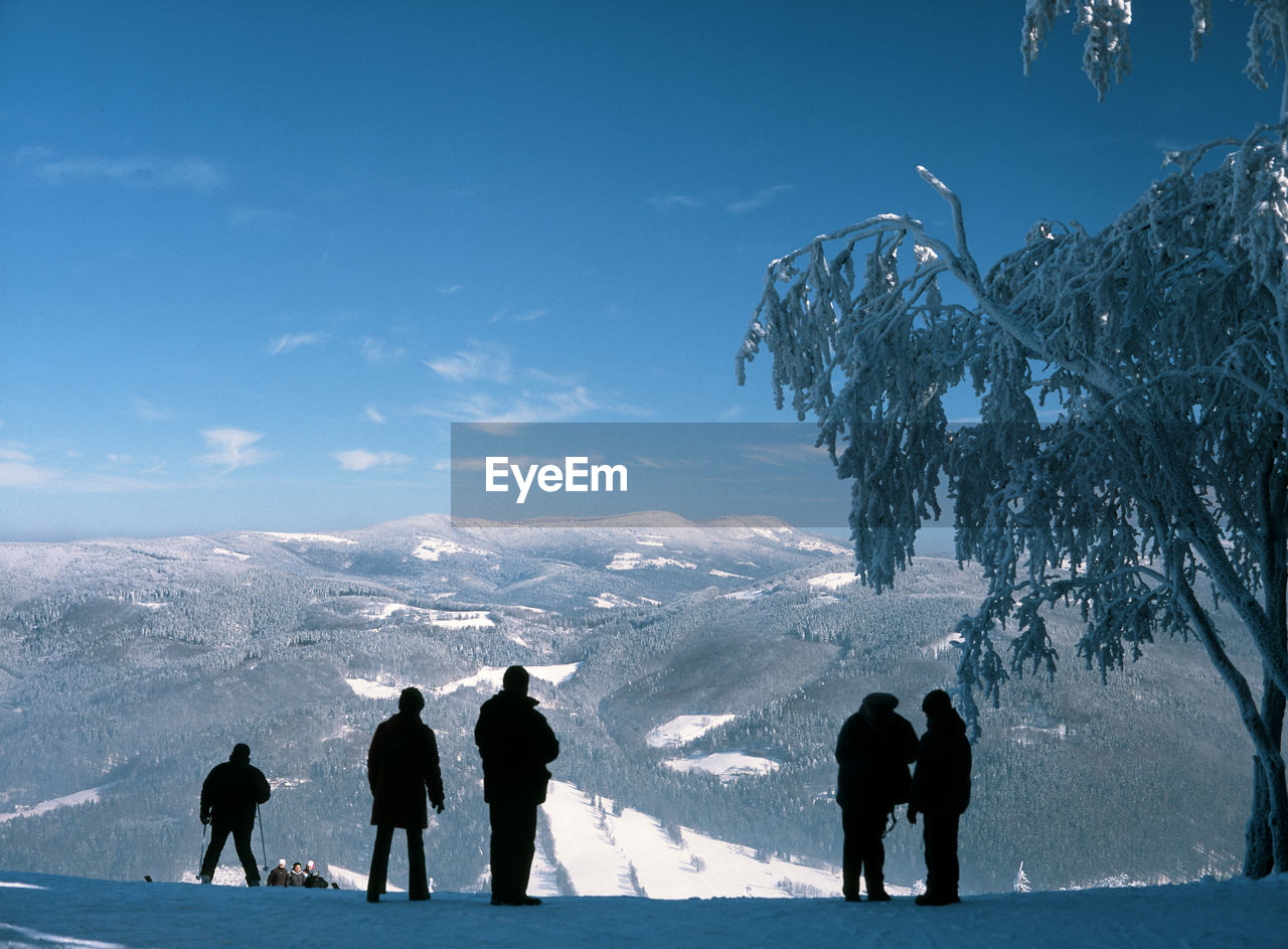 Silhouette people standing on snowcapped mountain against sky