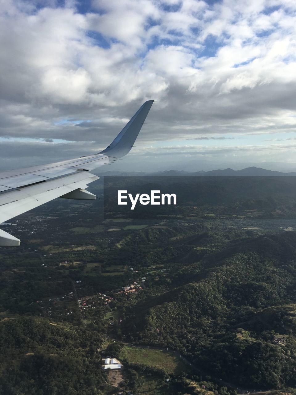 AIRPLANE FLYING OVER LANDSCAPE AGAINST SKY