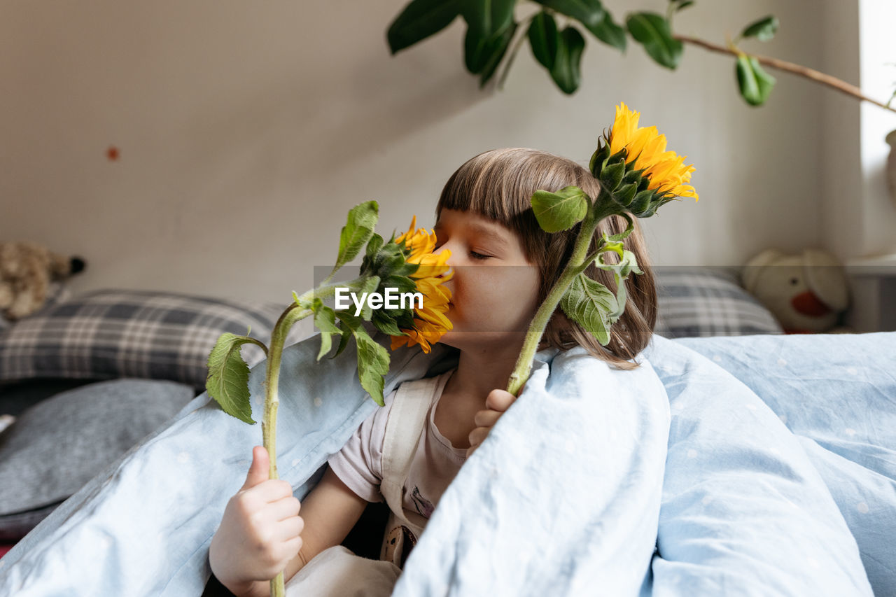 A toddler girl holding and smelling sunflowers