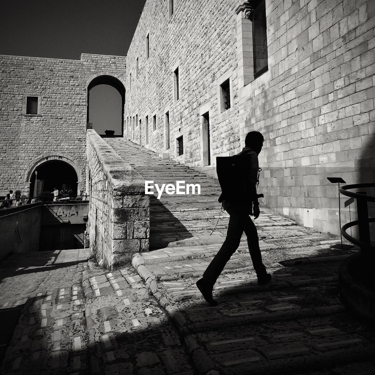 Side view of a silhouette man walking by stone wall