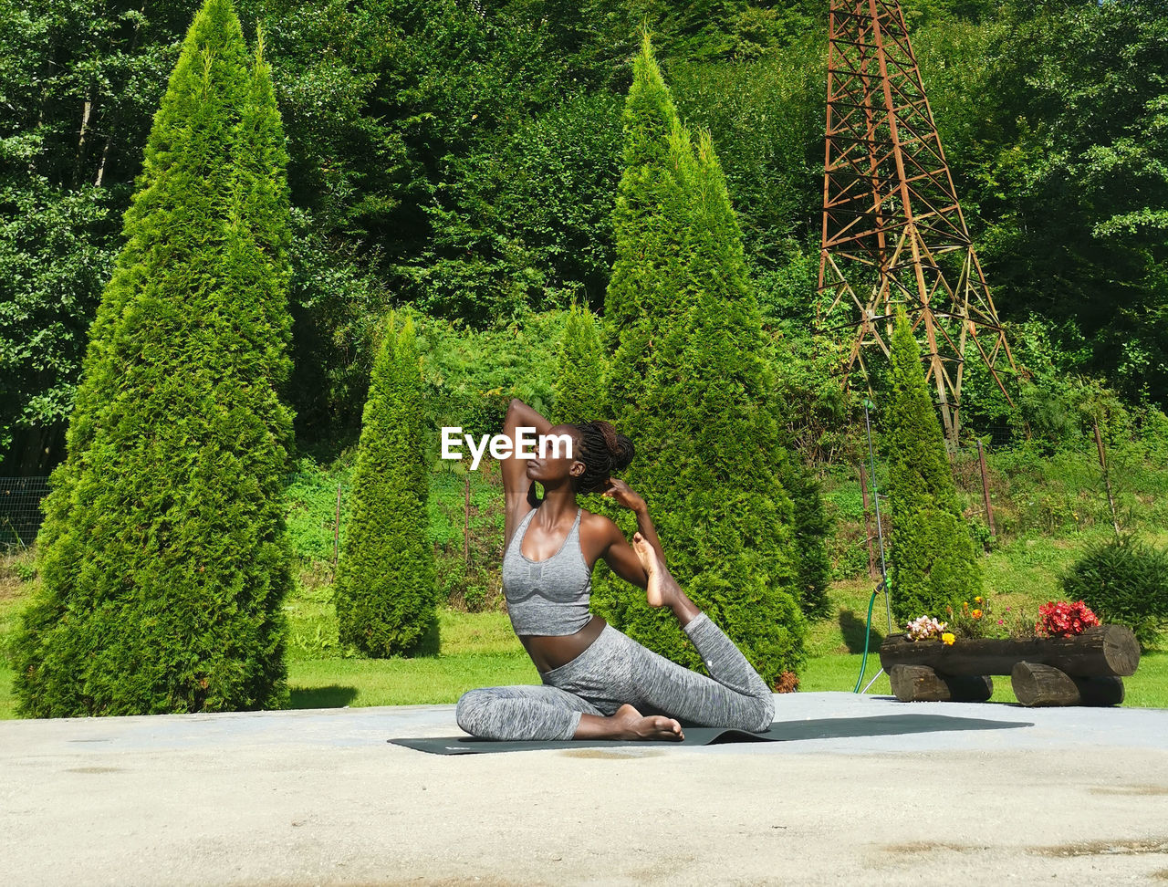 Side view of woman sitting on plant against trees