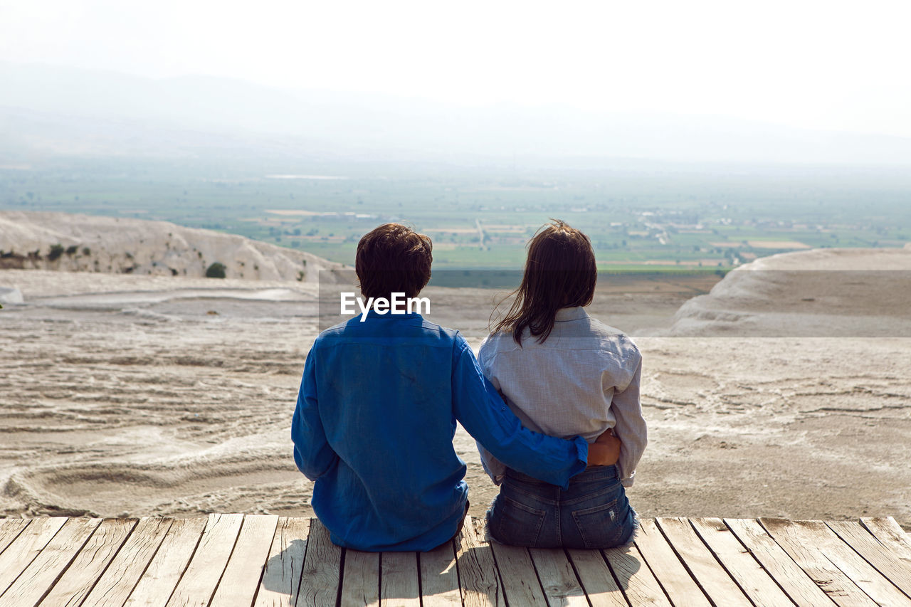 Couple man and woman sit back on a wooden floor in the street in pamukkale and look 
