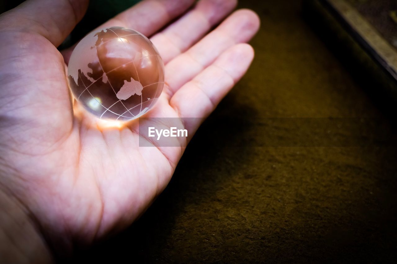 Cropped hand of person holding crystal ball on table
