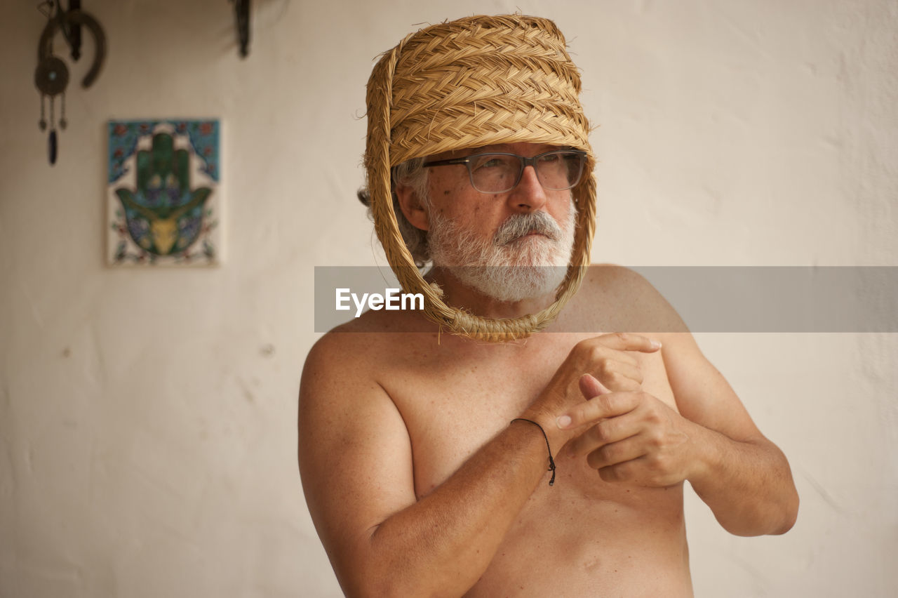 Shirtless senior man wearing wicker basket at home