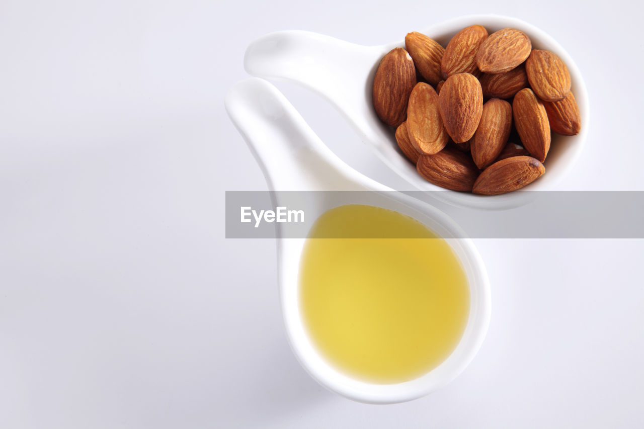 High angle view of almonds and oil in spoon over white background