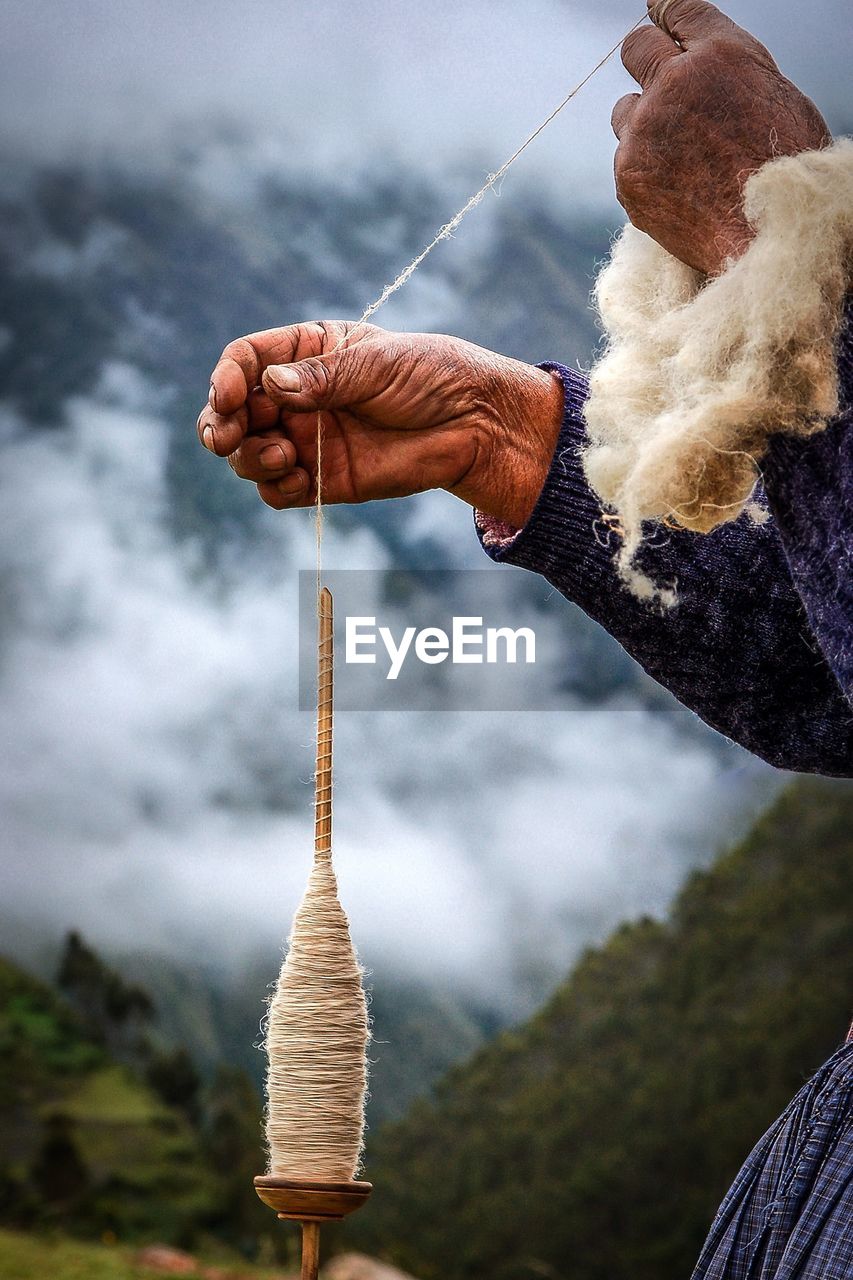 Cropped hands holding spool against mountains