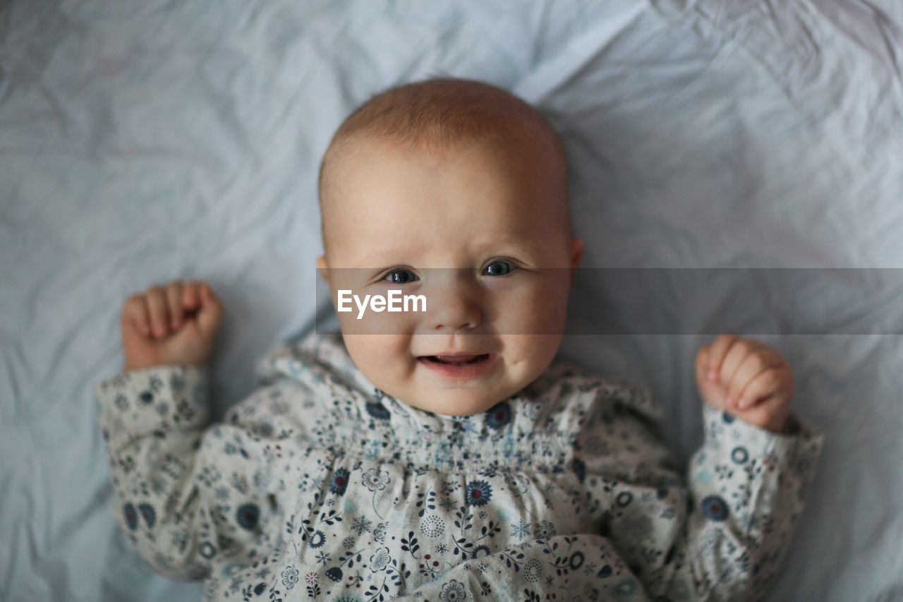 baby, child, portrait, childhood, indoors, innocence, one person, looking at camera, cute, person, emotion, smiling, furniture, baby clothing, happiness, bed, babyhood, clothing, front view, beginnings, lying down, skin, toddler, positive emotion, domestic room, cheerful, bedroom, high angle view, headshot, waist up, portrait photography, close-up, relaxation, lying on back, lifestyles, human face, domestic life, eye, gray