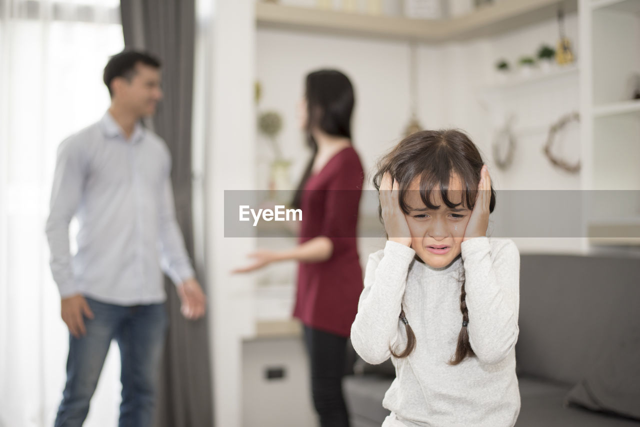 Close-up of girl crying while parents fighting in background at home