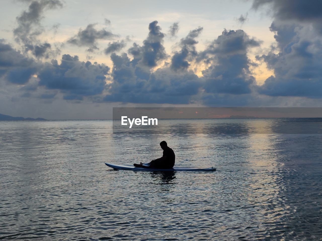 silhouette man on boat in sea against cloudy sky during sunset