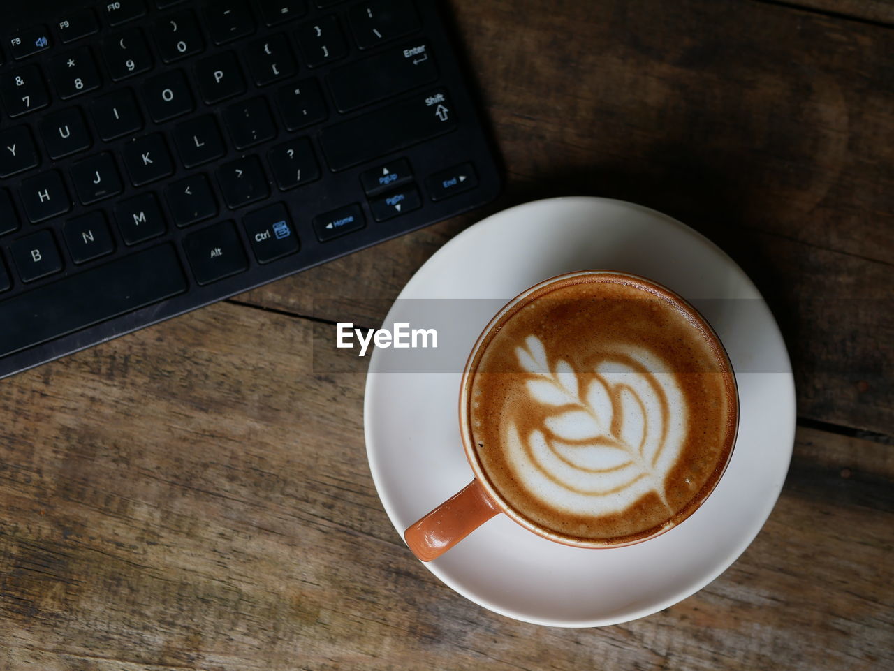 One cup of coffe latte with wooden and keyboard background 