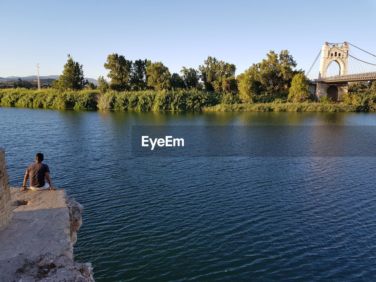 Rear view of man sitting by river against sky