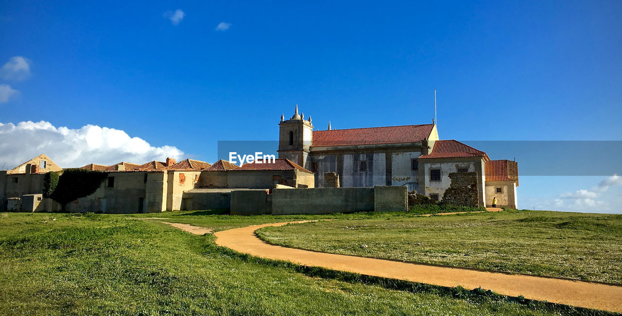 Footpath on grassy field leading towards houses against sky
