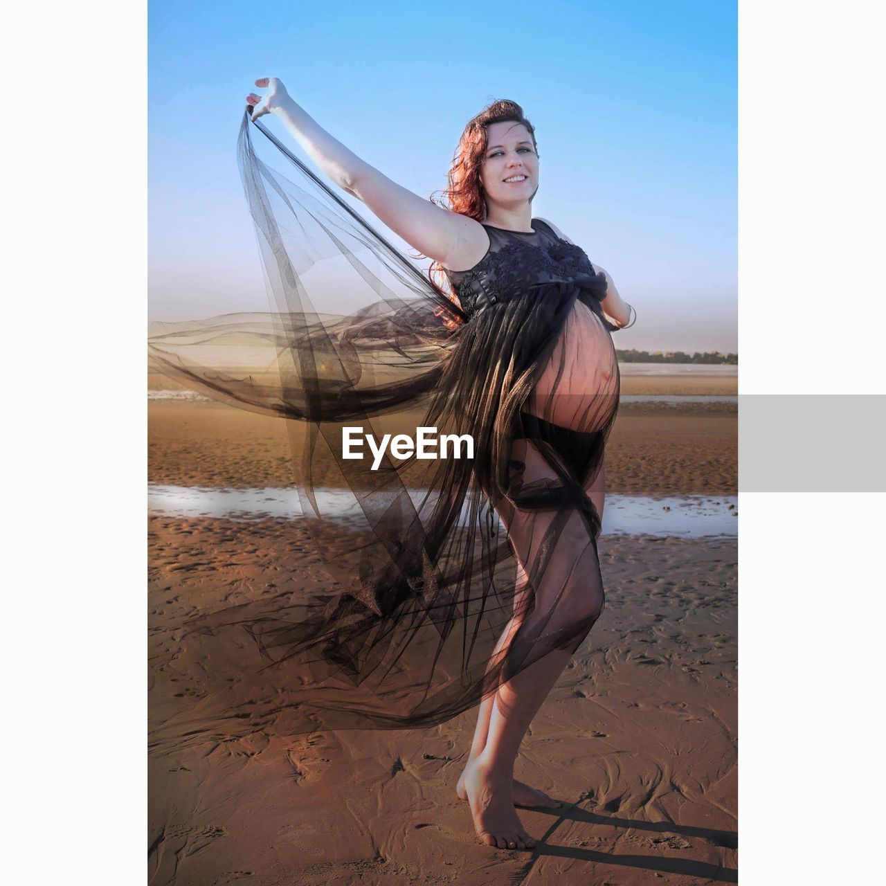 Pregnant woman standing at beach against sky during sunset