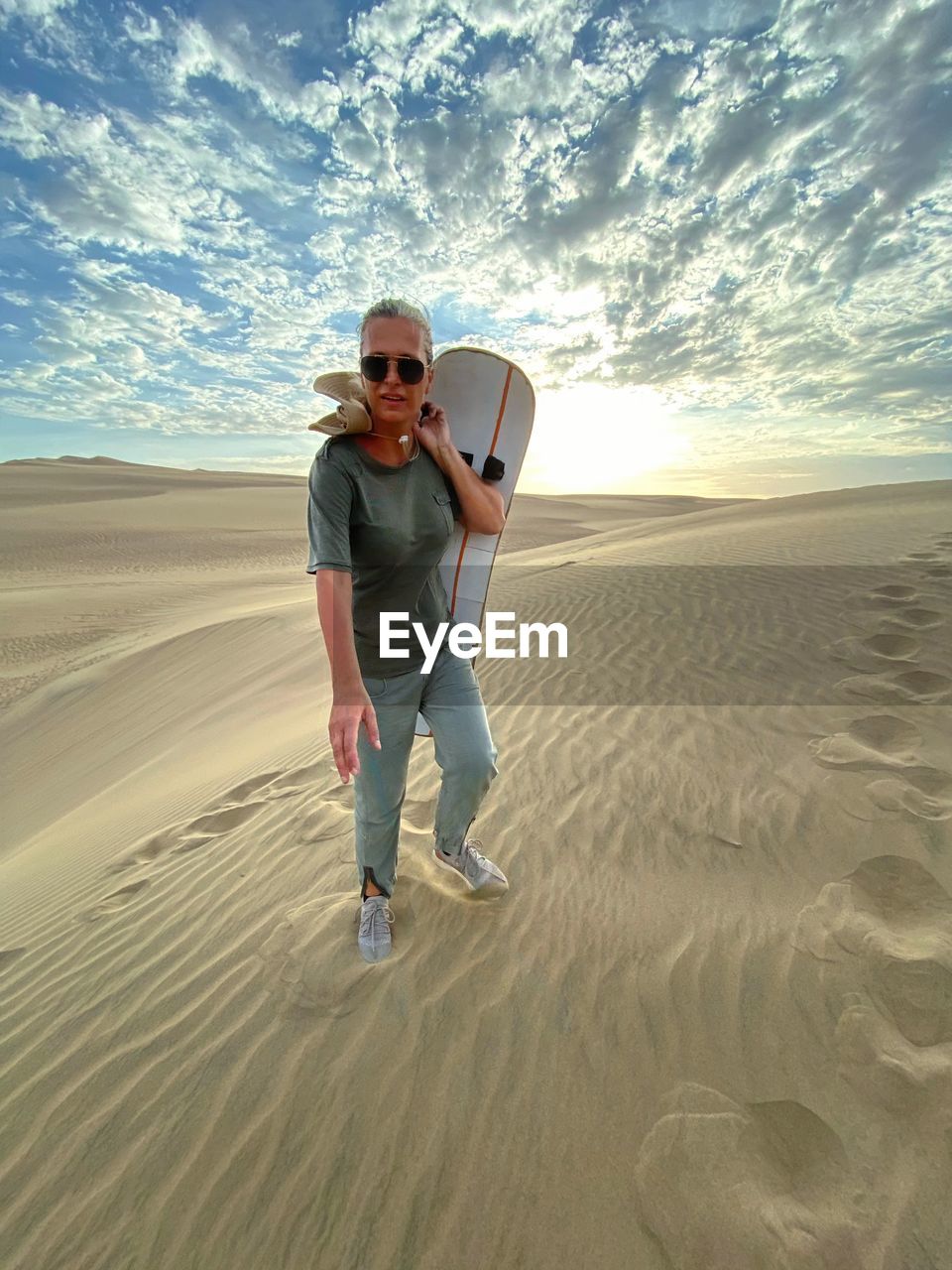 Full length of woman holding sandboard at desert during sunset