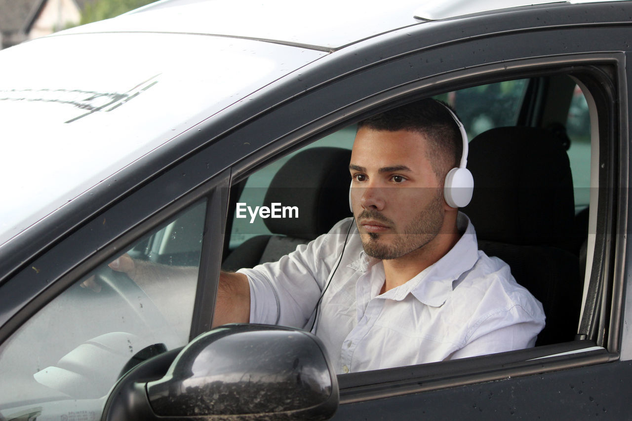Man wearing headphones driving car seen through window