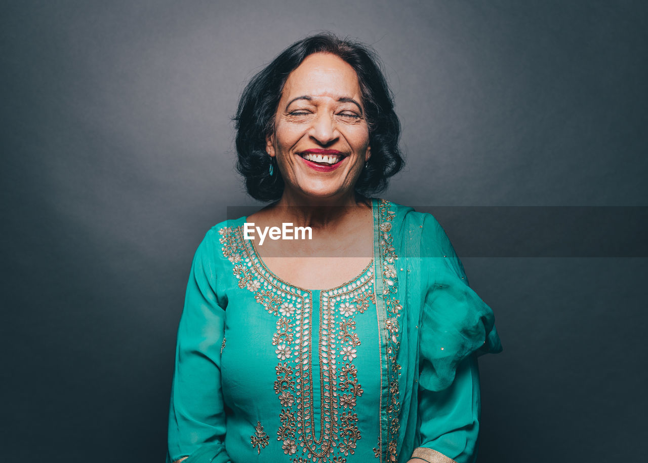 Smiling senior woman with eyes closed standing against gray background