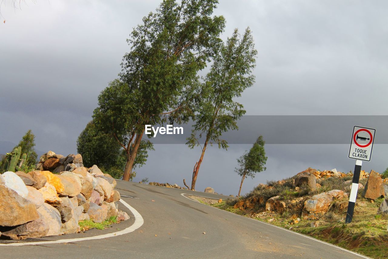 Tilt image of empty road by sign against cloudy sky