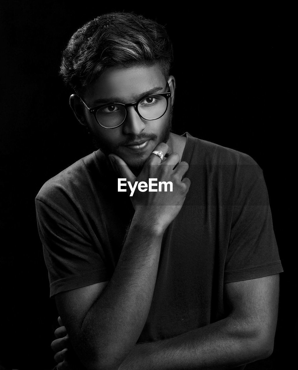 Thoughtful young man wearing eyeglasses against black background