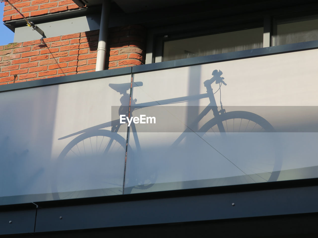 The shadow of a bicycle placed behind glass on a balcony