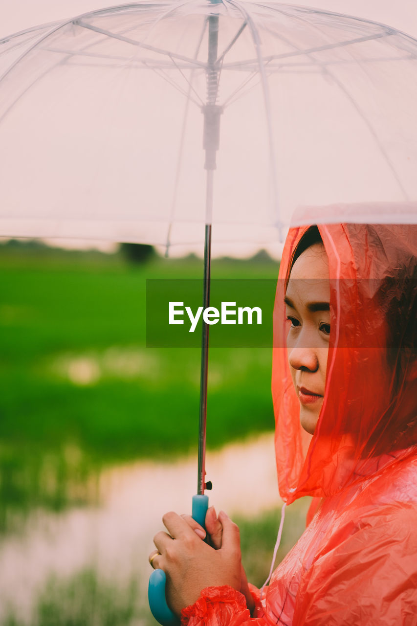 Side view of young woman carrying umbrella while standing on field during monsoon