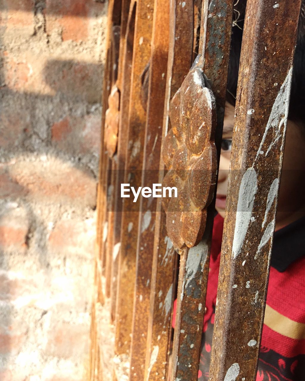 Close-up of boy looking through rusty metallic gate