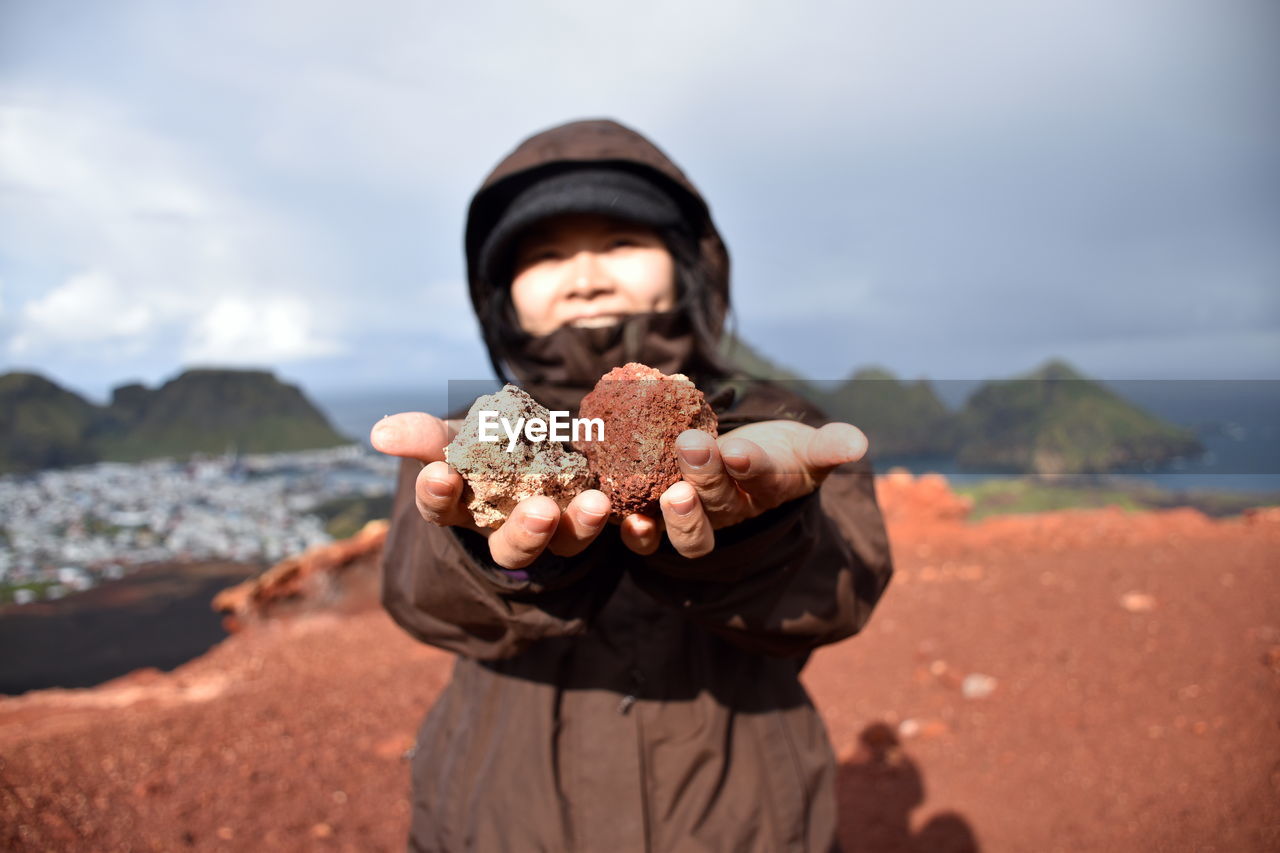 Smiling woman holding rocks while standing on mountain