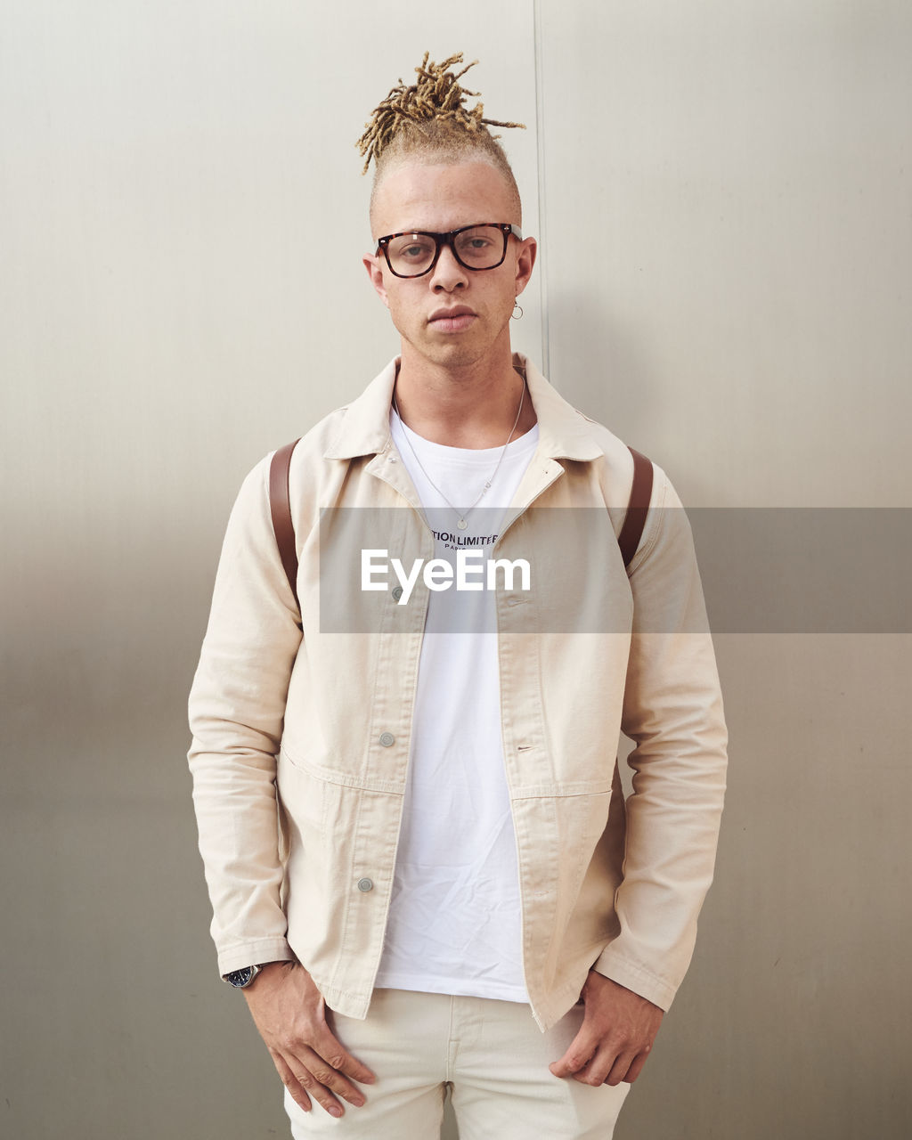 PORTRAIT OF YOUNG MAN WEARING EYEGLASSES STANDING AGAINST WALL