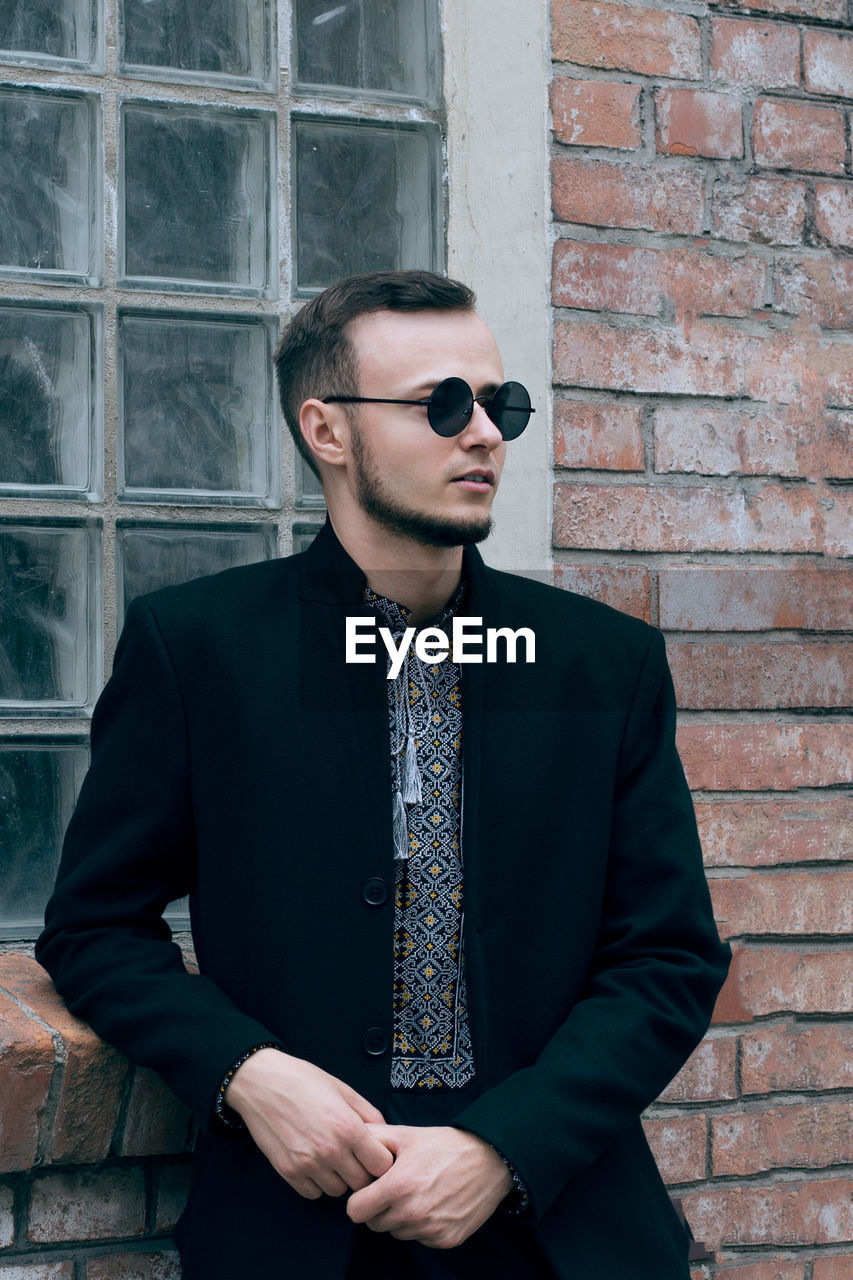 Young man wearing sunglasses while standing against brick wall