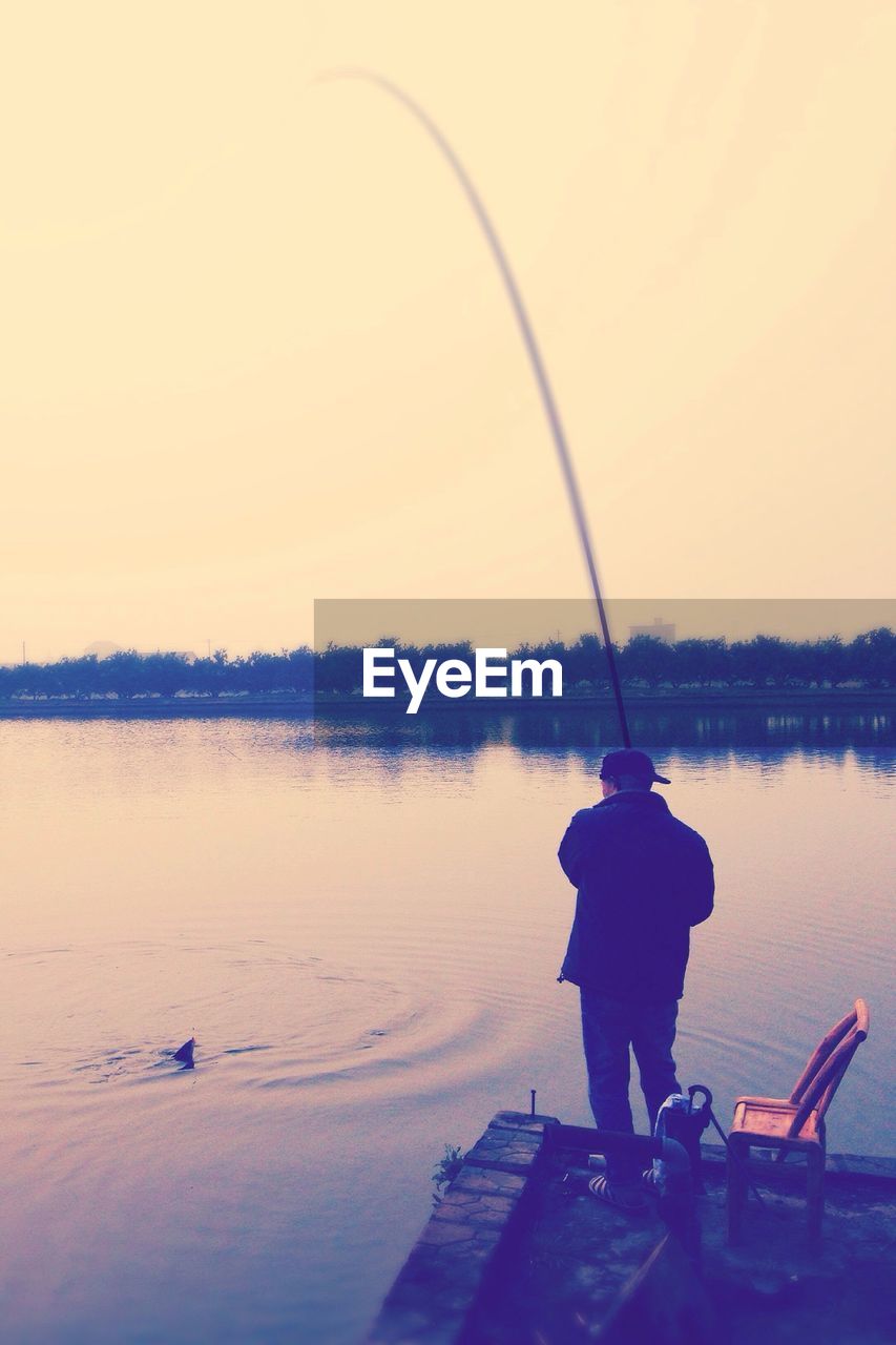 Rear view of man fishing on lake against clear sky