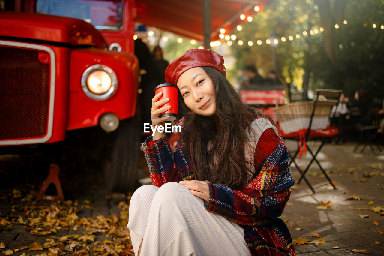 Beautiful asian woman in plaid coat and red leather hat on street with coffee