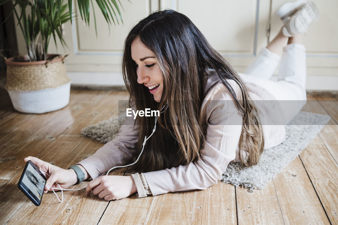 Beautiful woman having video call with friend while lying on floor at home