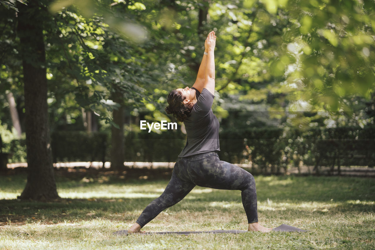 Side view of overweight female standing in ashta chandrasana pose while practicing yoga on mat in sunlight