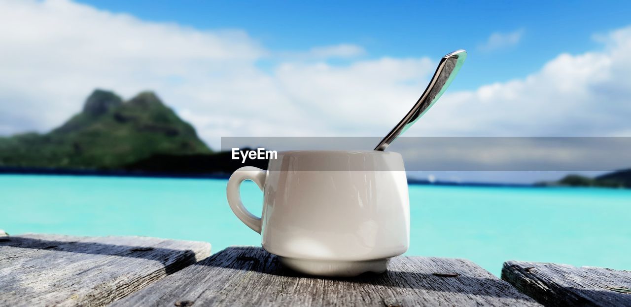 Close-up of cup on wood against sky