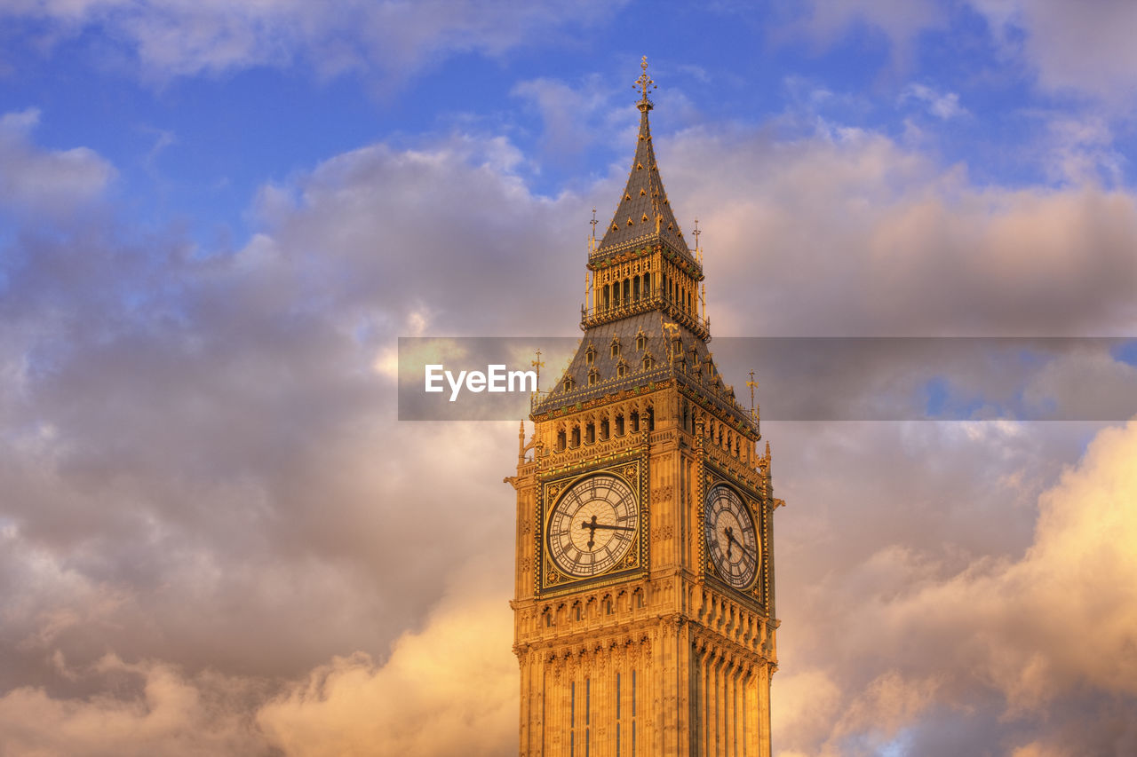 LOW ANGLE VIEW OF CLOCK TOWER AMIDST BUILDINGS AGAINST CLOUDY SKY