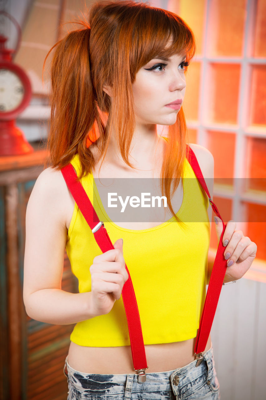 Beautiful young woman wearing suspenders standing indoors