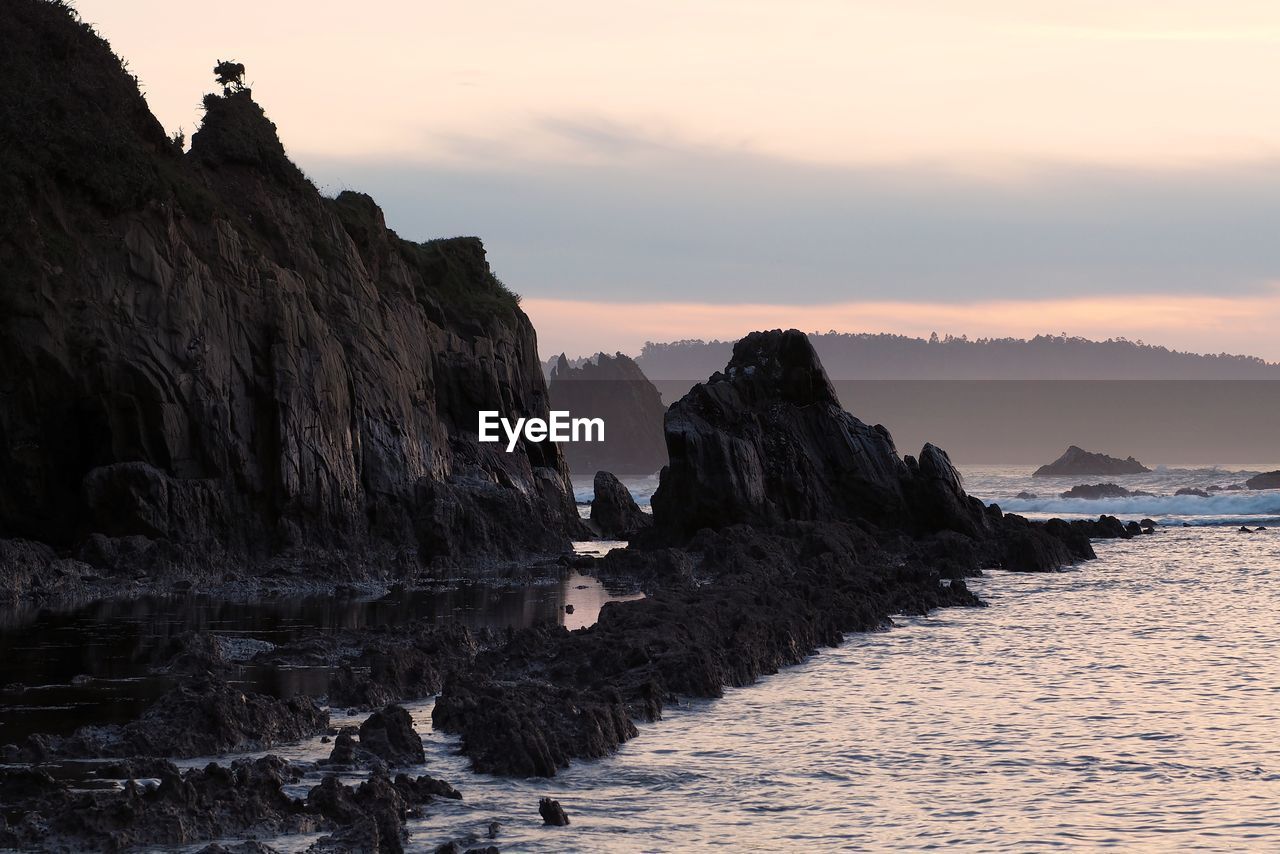 Rock formations by sea against sky during sunset