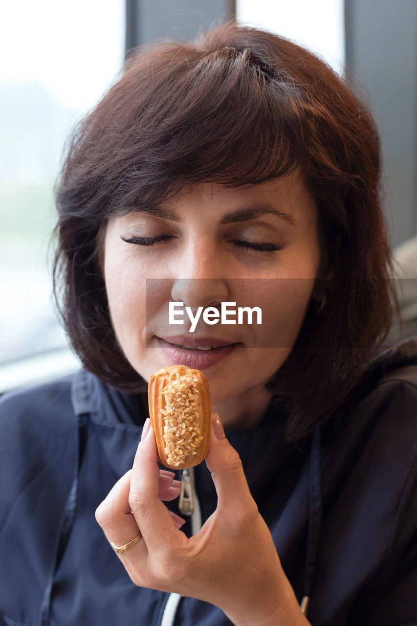 A beautiful adult woman in a cafe is happy to try a mini eclair cake.