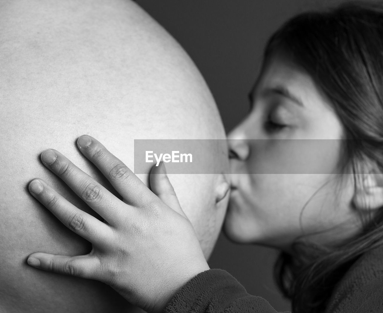 Close-up of girl kissing pregnant mother abdomen