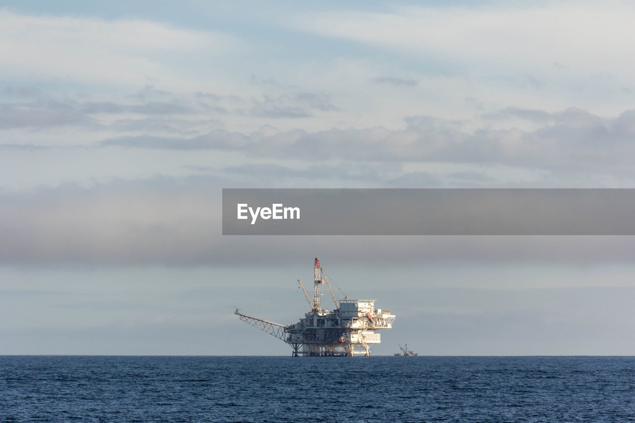 Offshore platform in sea against cloudy sky
