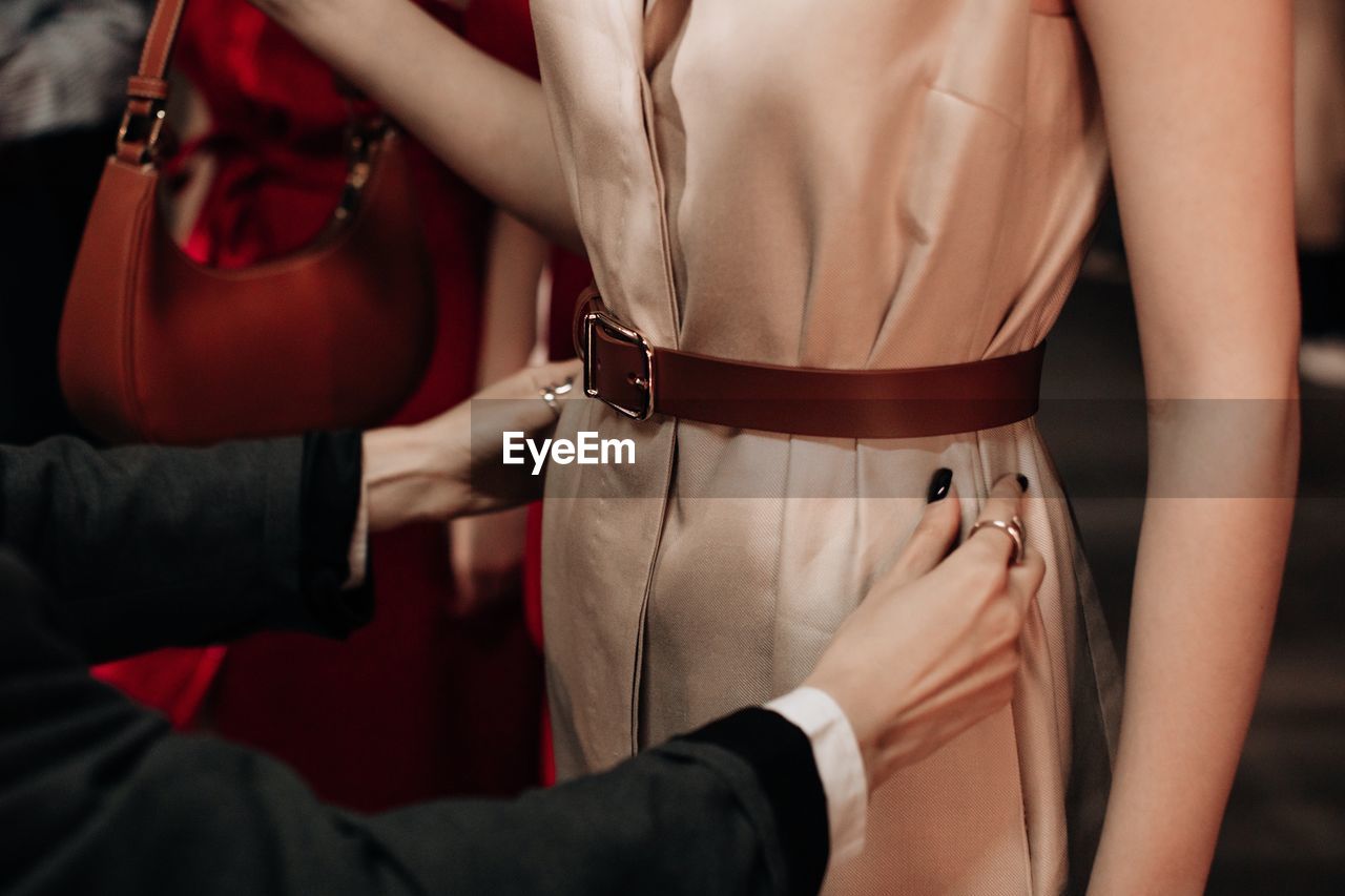 Female hands preparing fashion model dressed in beige long dress with brown belt