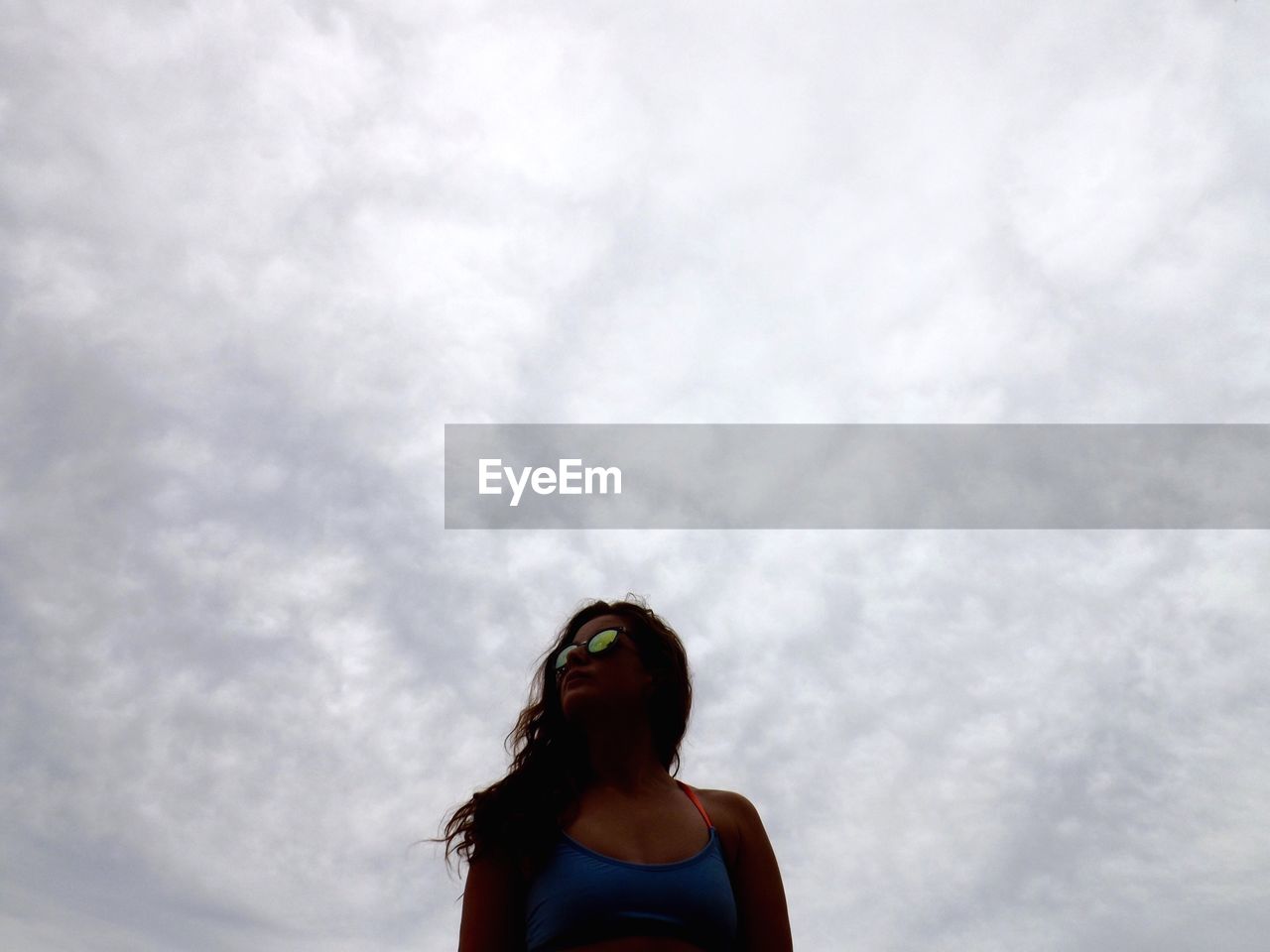 Low angle view of woman wearing sunglasses against cloudy sky
