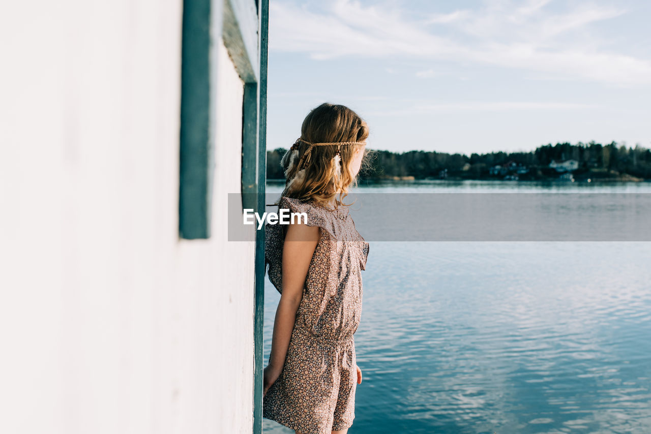 Young girl with a feather headband looking out to sea whilst playing