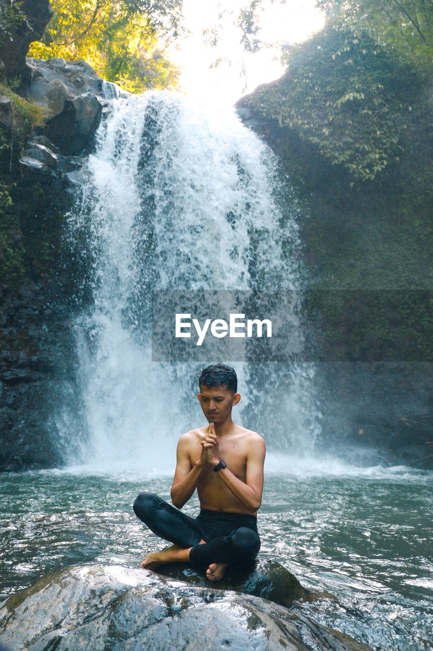 Full length of shirtless man splashing water in rocks