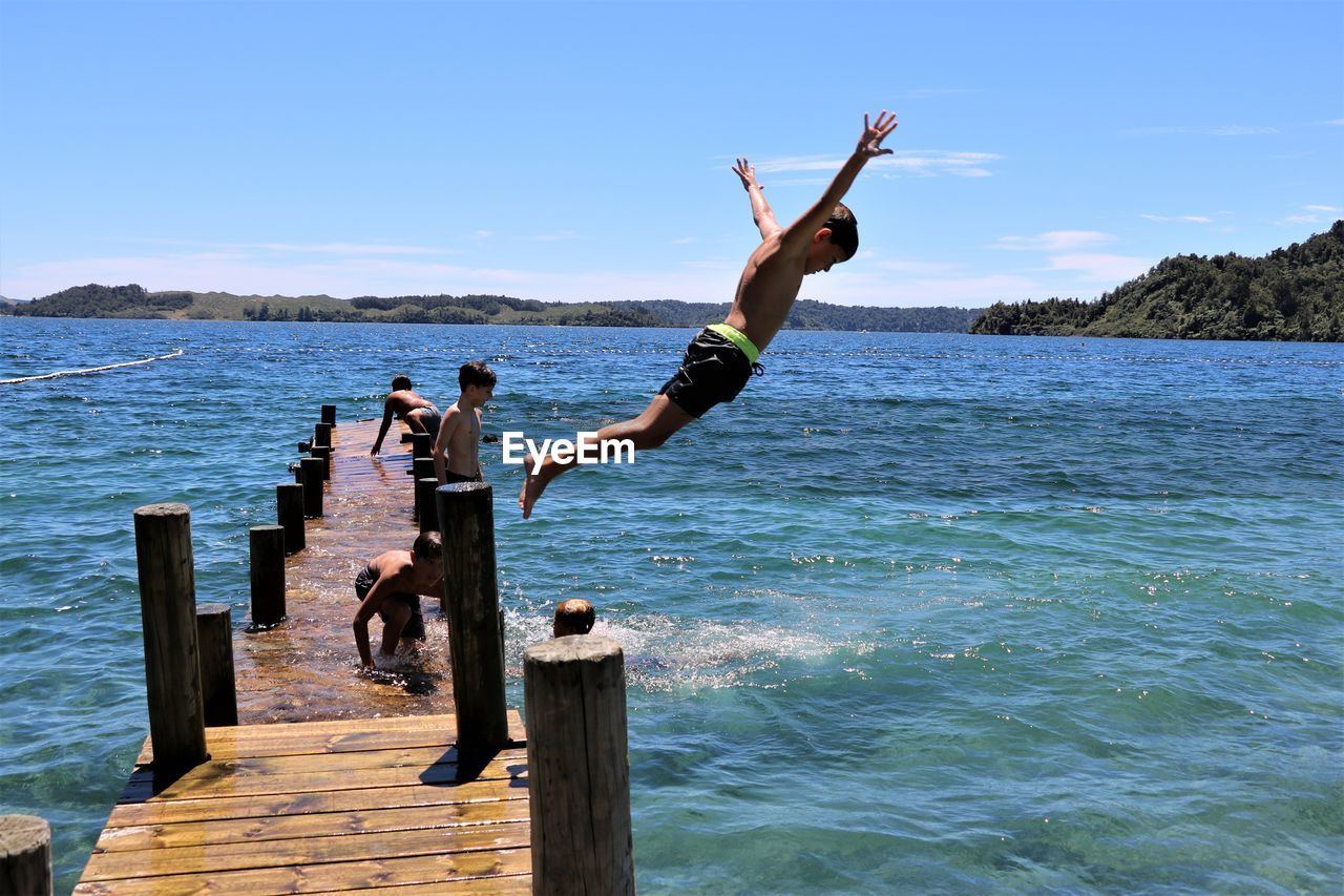 People jumping from pier in sea against sky