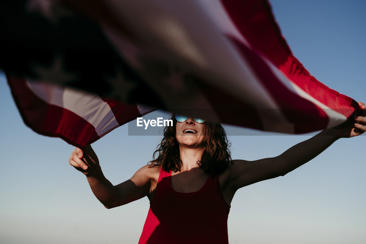 Low angle view of woman with american flag against clear blue sky